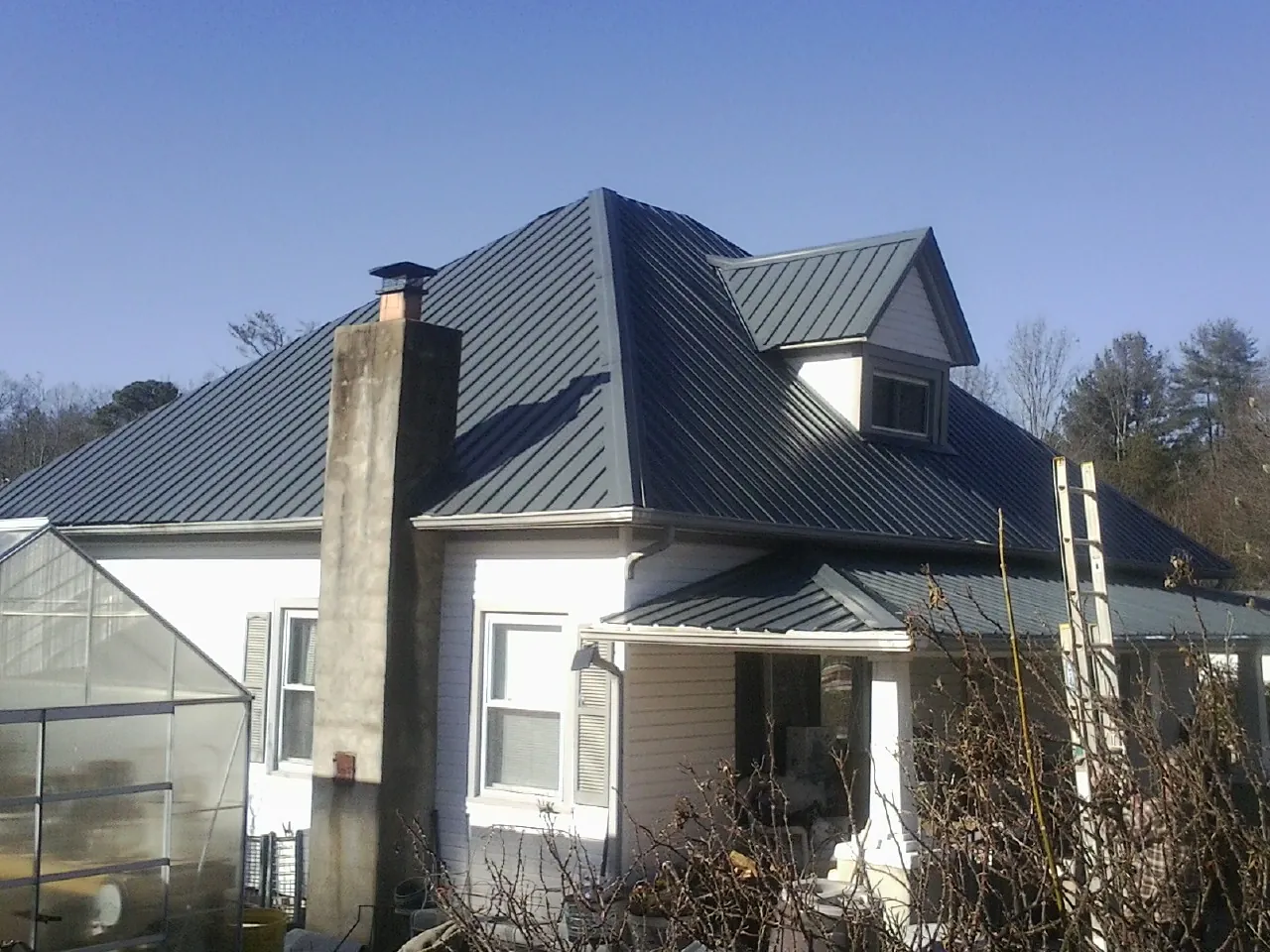 Dark blue standing seam metal roof on a white farmhouse with dormer — Slate & Tile Roof Repair by Roofing Brothers in Quebeck