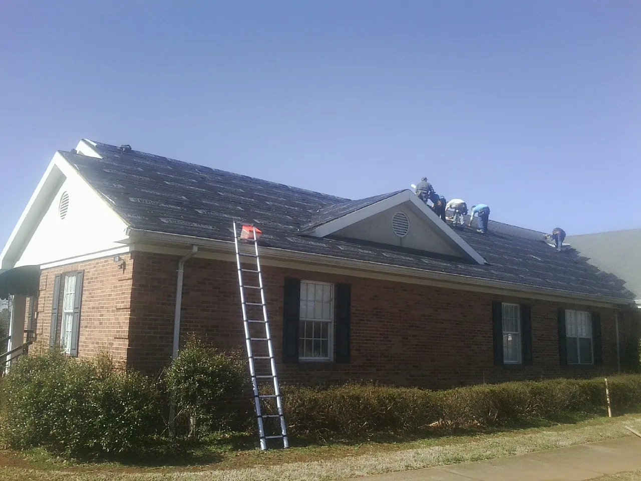 Crew tearing shingles off a brick ranch roof with a ladder set — Emergency Roof Repair work by our crew in Quebeck