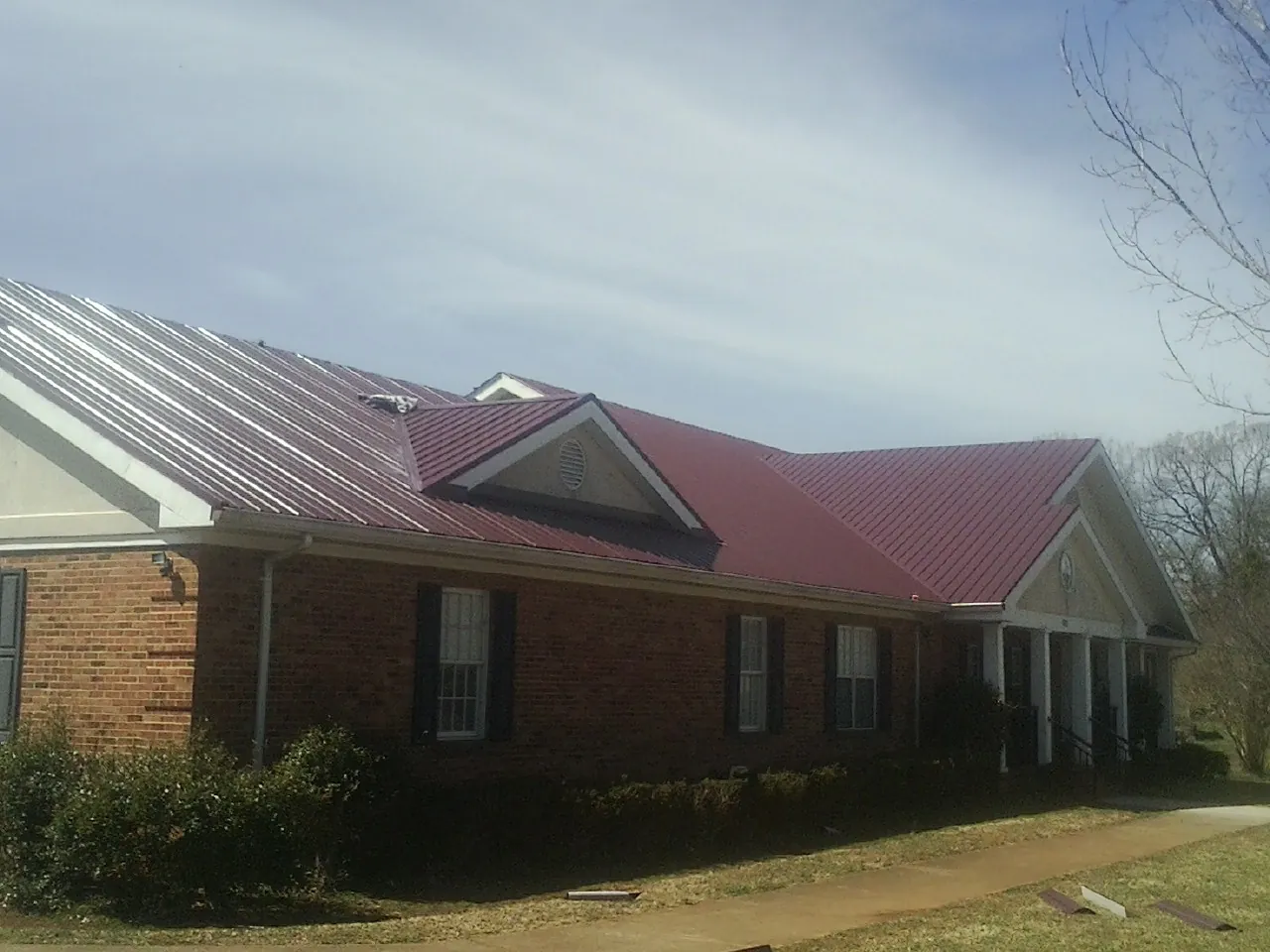 Red metal roof with gabled entries on a long brick building, from a Hail Damage Roof Repair job in Quebeck