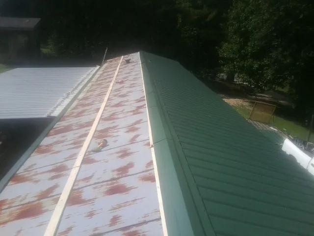 Old rusted panels beside newly installed green metal roofing — Wind Damage Roof Repair by Roofing Brothers in Quebeck