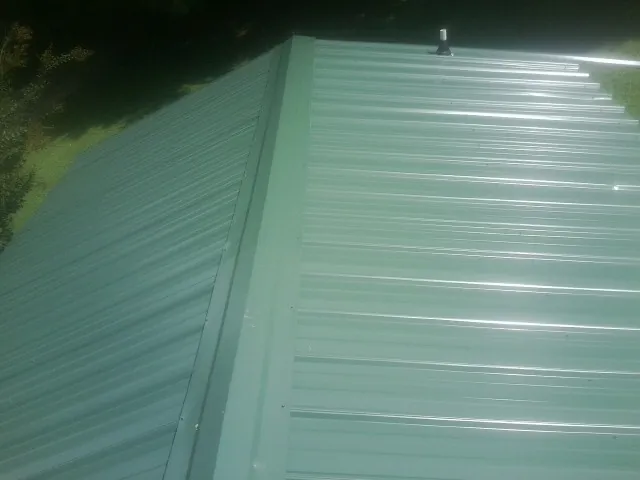 New green metal panels meeting at the ridge of a roof — Flat Roof Repair work by our crew in Quebeck