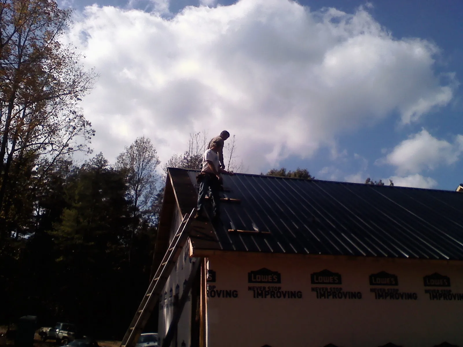 Roofer fastening dark metal panels high against a cloudy sky, from a Roof Inspection job in Quebeck