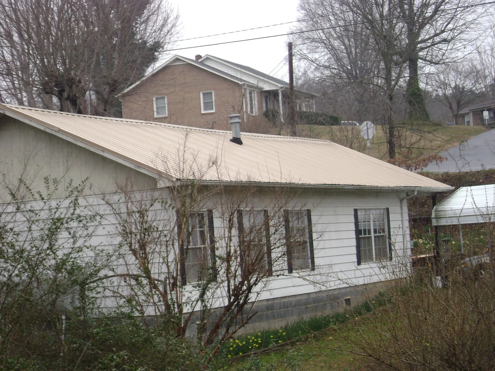 Tan metal roof on a white sided house set into a hillside — Commercial Roofing by Roofing Brothers in Quebeck