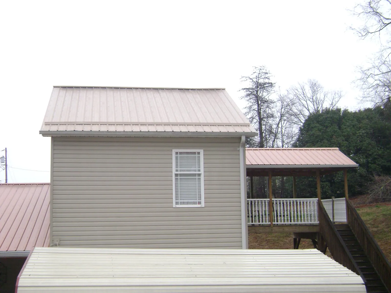 Tan metal roofs on a two story addition and attached porch, from a Roof Replacement job in Quebeck